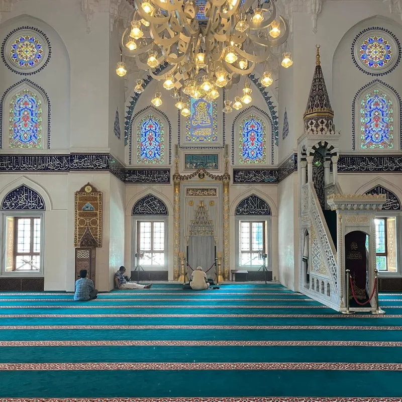 Quiet mosque interior with stained glass windows and teal carpet