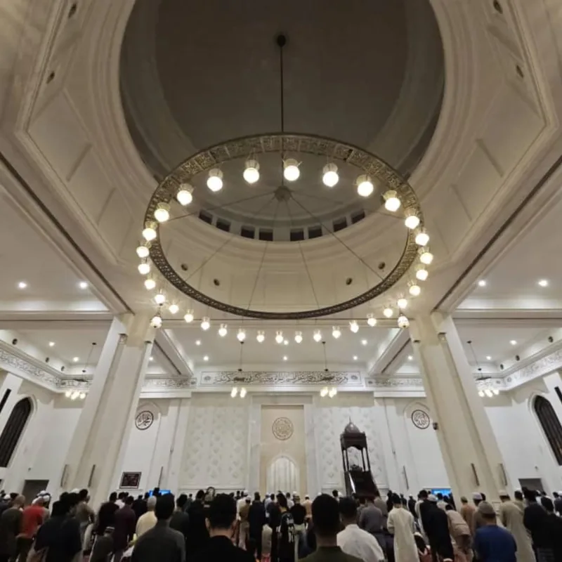 Congregation praying beneath a grand domed ceiling and chandelier